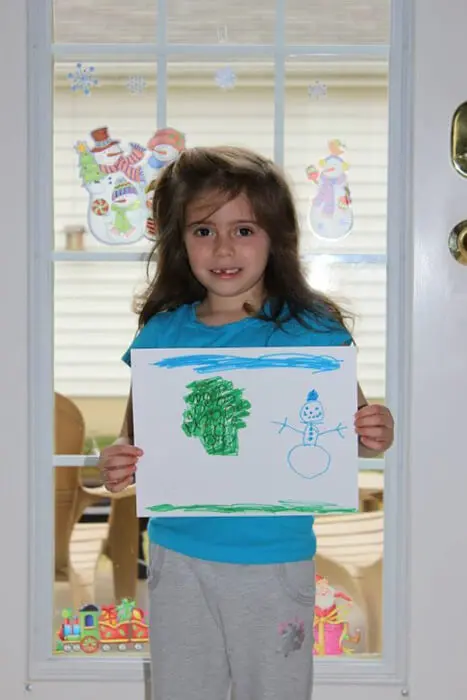 Child holding a winter scene drawing for the Alexandria Children's Dentistry Holiday Art Raffle