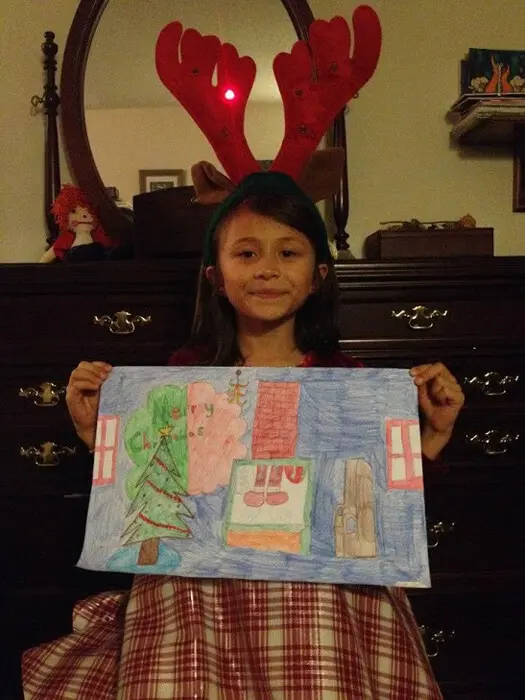 Child wearing reindeer antlers displaying a holiday drawing for the Alexandria Children's Dentistry Holiday Art Raffle