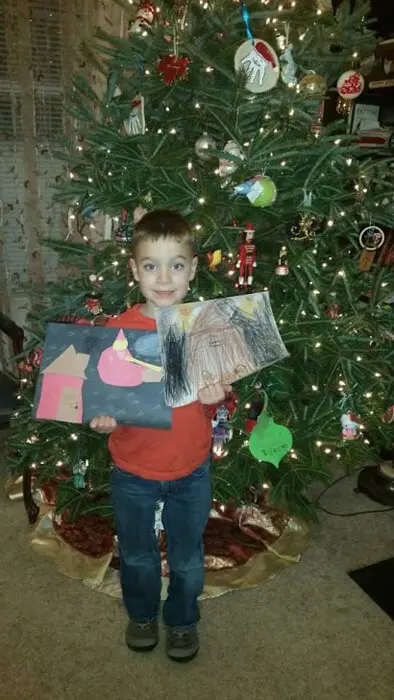 Child holding a holiday drawing in front of a Christmas tree for the Alexandria Children's Dentistry Holiday Art Raffle