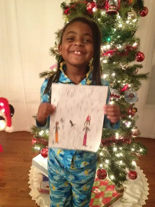 Child proudly displaying festive holiday artwork for the Alexandria Children's Dentistry Holiday Art Raffle