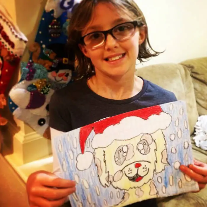Child proudly displaying a Christmas-themed drawing for the Alexandria Children's Dentistry Holiday Art Raffle