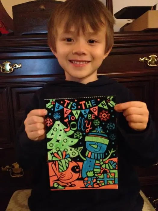 Child holding a festive Christmas artwork for the Alexandria Children's Dentistry Holiday Art Raffle