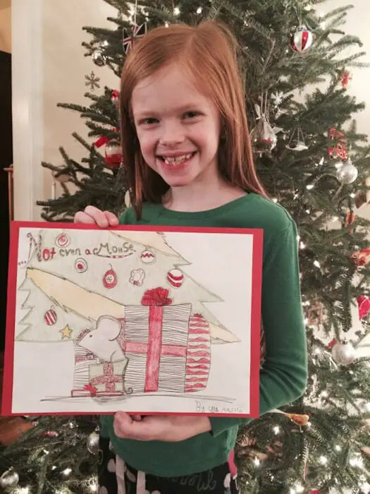 Child smiling while holding a Christmas house drawing for the Alexandria Children's Dentistry Holiday Art Raffle
